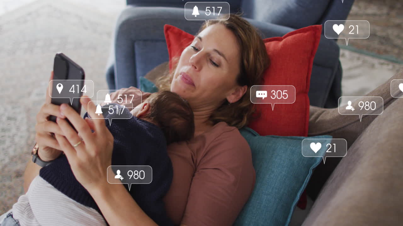 animación de iconos de redes sociales con números sobre mujer caucásica sosteniendo un bebé y usando un teléfono inteligente