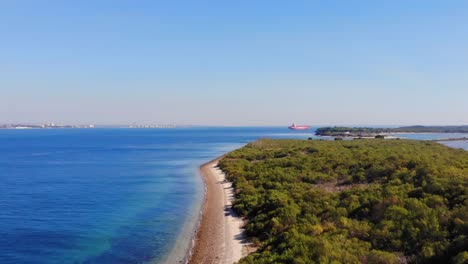 drone shot rising and filming land and water with an anchored tanker ship in the bay