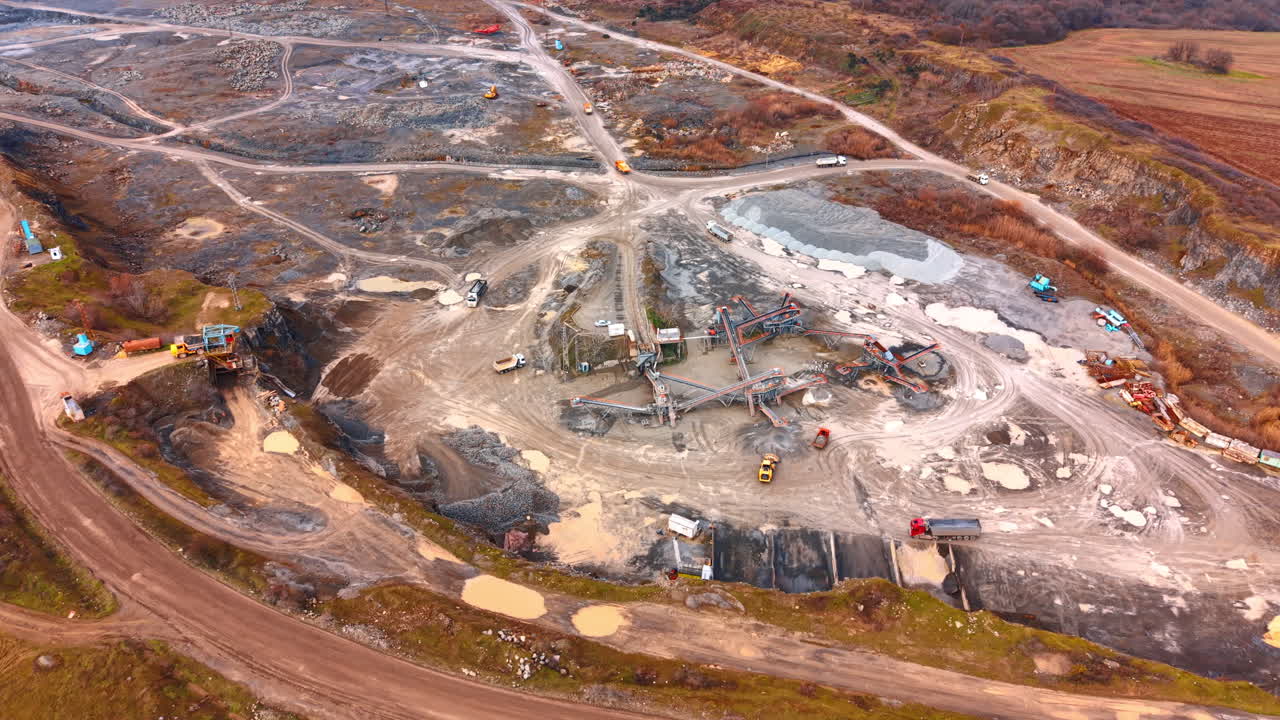 Aerial view of stone crushing plant and industrial quarry. Wide high angle view of mining equipment, conveyor belts, and trucks in a gravel quarry