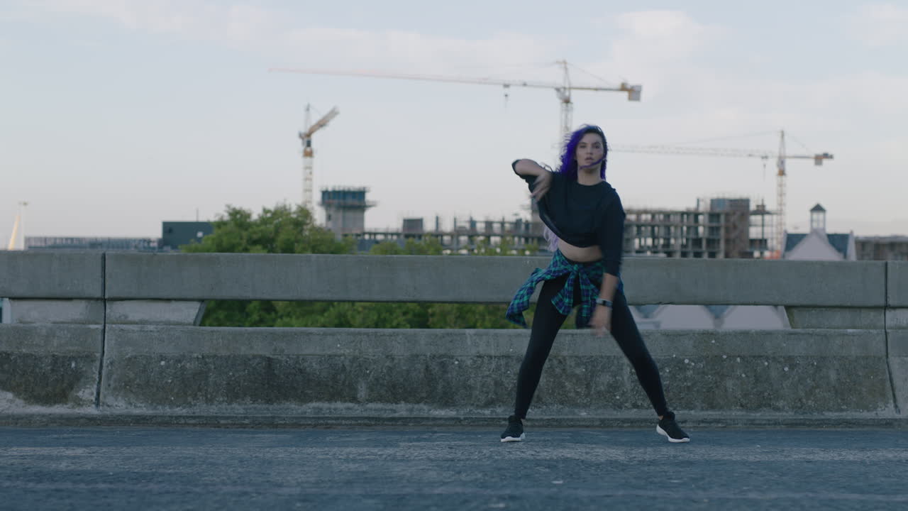 bailarina hermosa bailarina joven realizando baile callejero de estilo urbano en la ciudad practicando movimientos de estilo libre con cabello púrpura