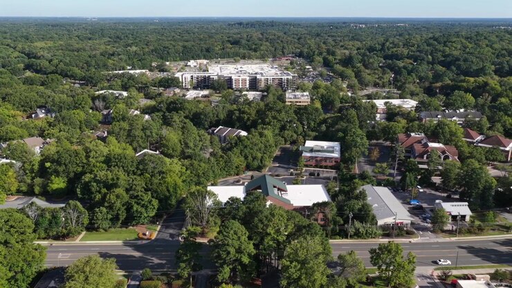 Un secondo complesso residenziale boscoso si estende sotto una fitta copertura arborea vicino alla Duke University a Durham, in Carolina del Nord, con uno sviluppo a uso misto visibile sulla cresta retrostante. Vista aerea