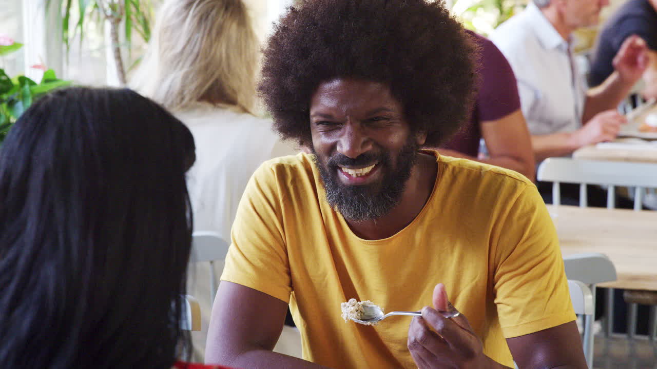 Middle aged black man eating breakfast and talking with his girlfriend at a restaurant, her back to the camera