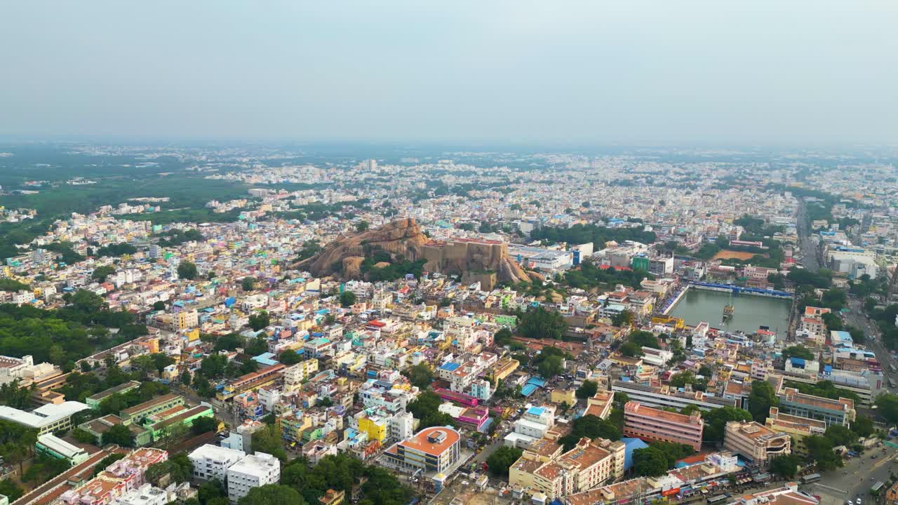 Malaikottai rock fort in middle of Tiruchirappalli city's dense urban buildings, aerial panoramic dolly