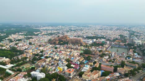 Fuerte-De-Roca-Malaikottai-En-Medio-De-Los-Densos-Edificios-Urbanos-De-La-Ciudad-De-Tiruchirappalli,-Plataforma-Rodante-Panorámica-Aérea