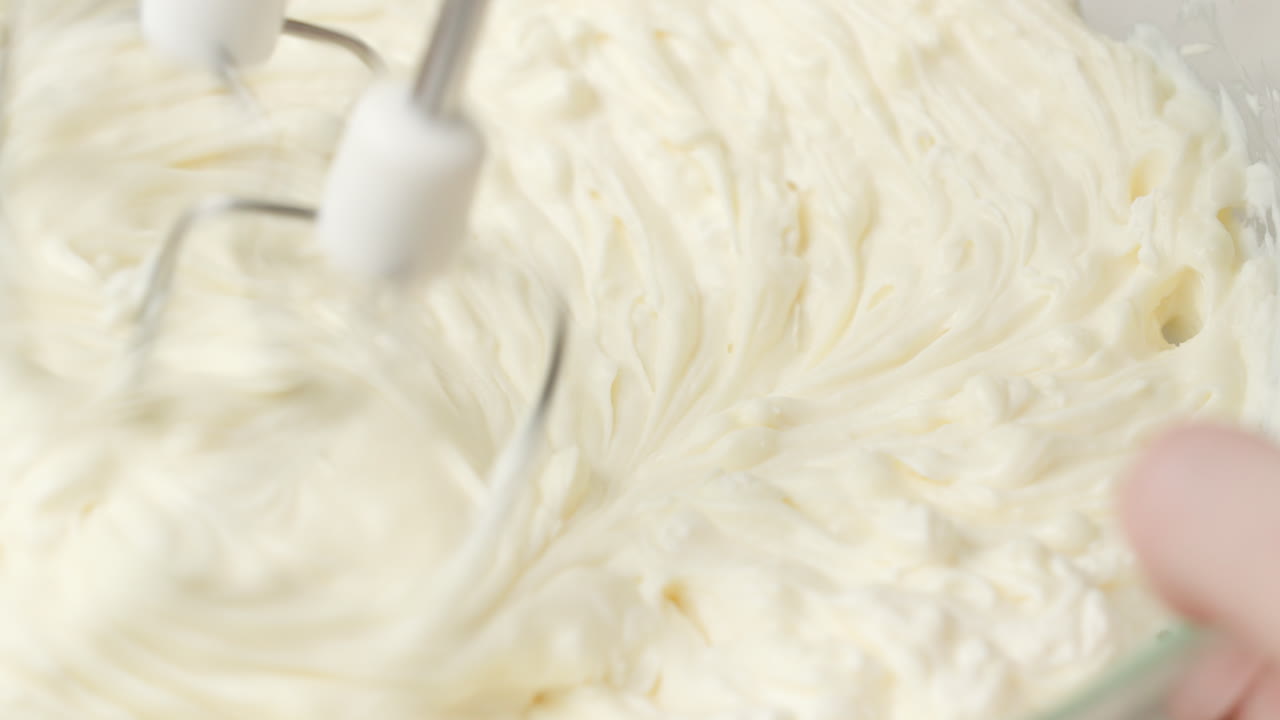 крупный план взбивания тяжелых сливок в стеклянной чаше ручным миксером до образования жестких пиков