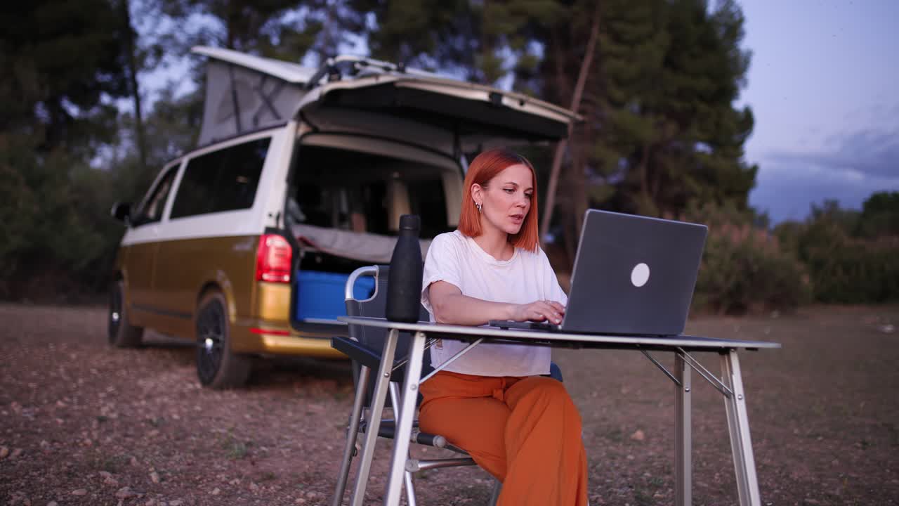 Giovane donna che lavora al laptop all'aperto, accanto a un camper.