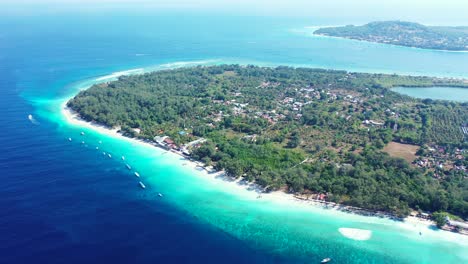 Low-tropical-island-with-trees-and-villages,-surrounded-by-white-beach-and-large-turquoise-lagoon-in-the-middle-of-deep-blue-sea-in-Indonesia