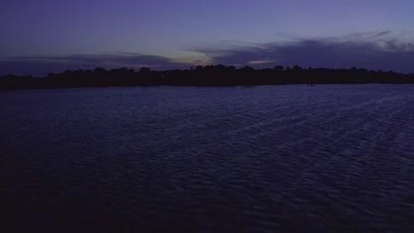 Wide-and-fast-aerial-shot-flying-across-pristine-summer-lake-at-twilight