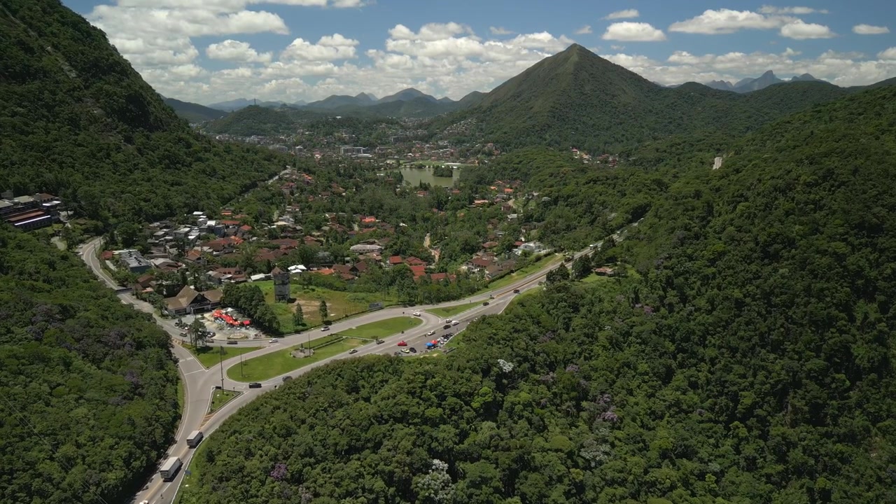 Acesso à cidade e à rodovia pedagiada de Teresópolis, mostrando a infraestrutura rodoviária cortando a selva com paisagem tropical ao fundo. Aproximação aérea descendente gravada em 4K a 25 fps.