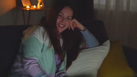 Smiling-Woman-Sitting-On-Sofa-At-Home-At-Night-Streaming-Or-Watching-Movie-Or-Show-On-Laptop