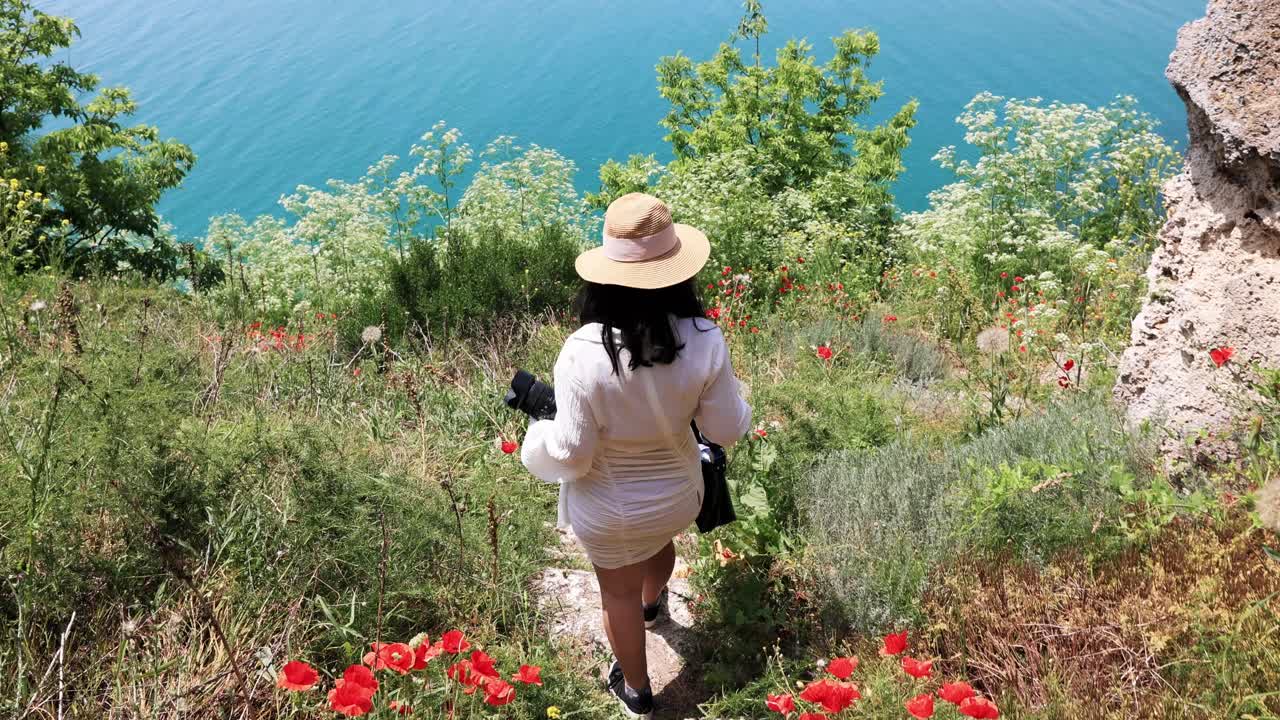 vista trasera de una mujer bajando las empinadas escaleras con flores de amapola en kaliakra, bulgaria