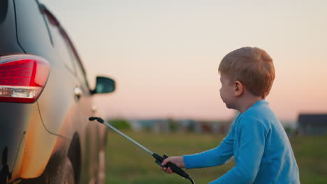 kid washes car with sprayer in meadow serious little boy cleans dirty automobile with water pumps at