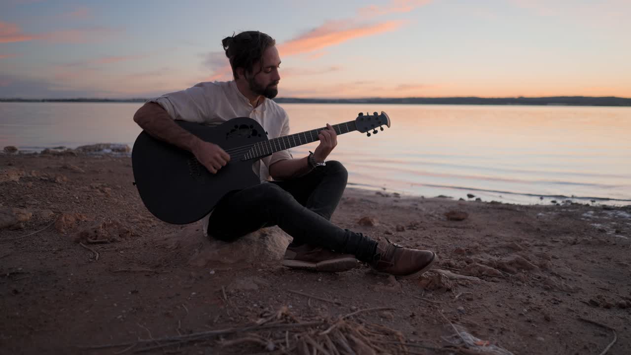 Man som spelar gitarr vid solnedgången vid sjön