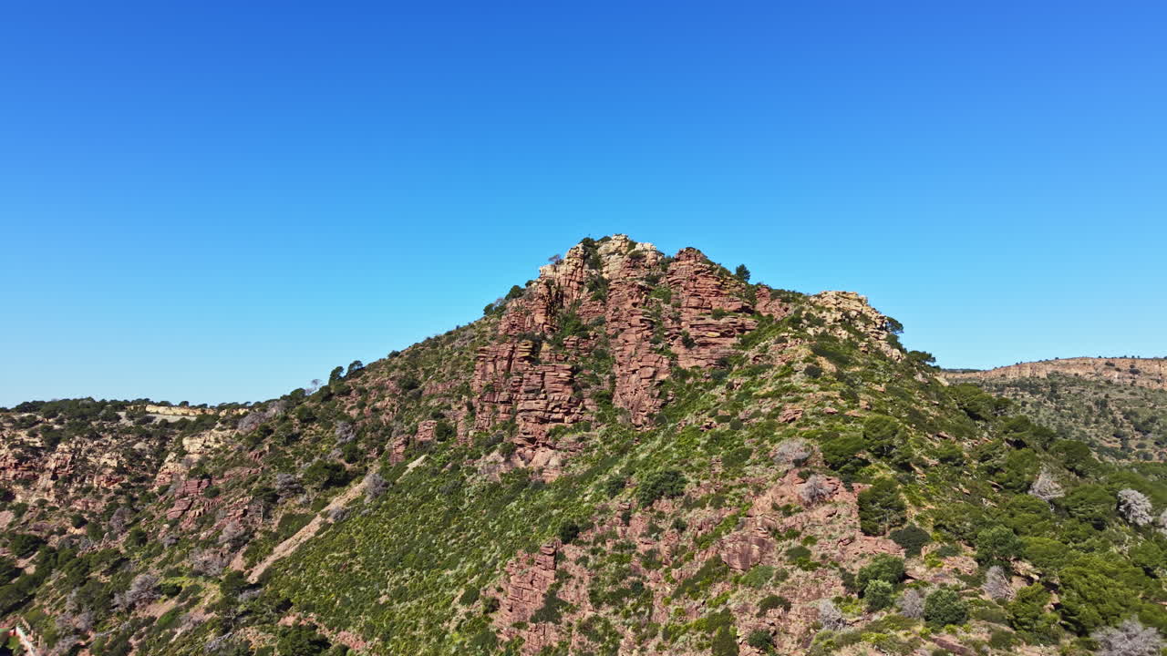Cresta montuosa con formazioni rocciose e vegetazione verde sotto un cielo azzurro e limpido durante il giorno, che mostra la bellezza naturale in un'area remota.