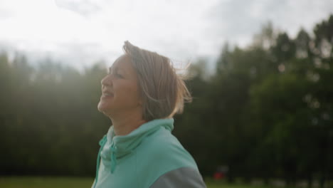 sport woman jogging energetically across open field, panting with joyful smile, hair flying in wind under bright sky, wearing athletic hoodie, radiating happiness and vitality