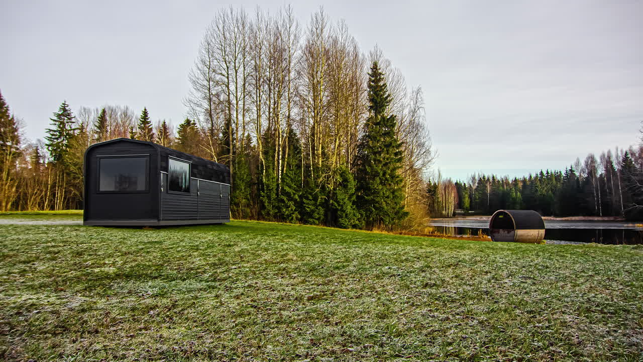 호수 옆에 있는 소박한 오두막과 배럴 사우나의 낮에서 밤까지의 시간 경과