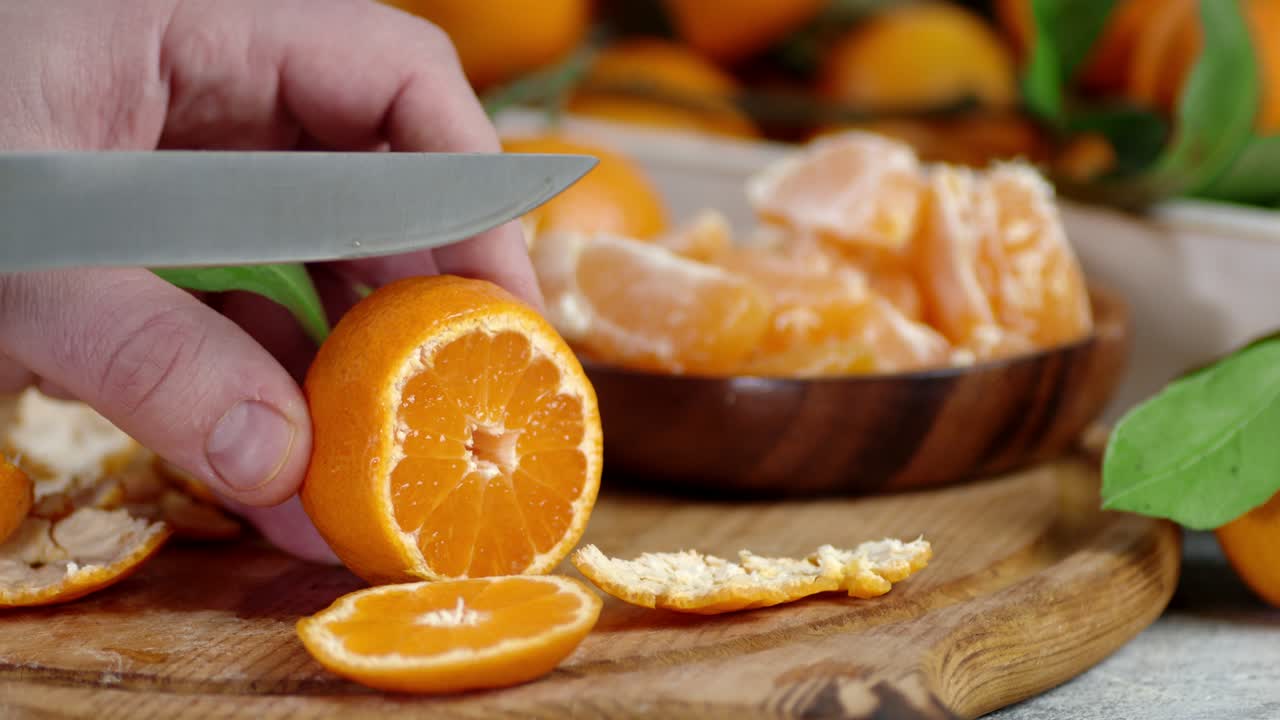 las manos de los hombres cortan una mandarina madura en pedazos redondos.