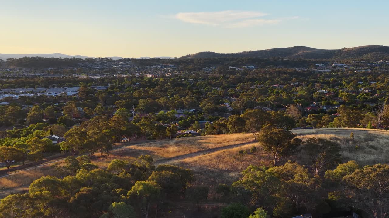 Ripresa aerea con drone su case residenziali e colline dorate a Canberra durante la calda luce del tramonto serale
