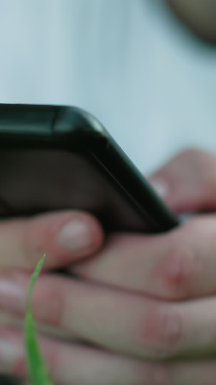 primer plano de un hombre tendido en un campo de hierba usando un teléfono inteligente, con enfoque en las manos sosteniendo el teléfono, el fondo natural borroso creando una atmósfera serena