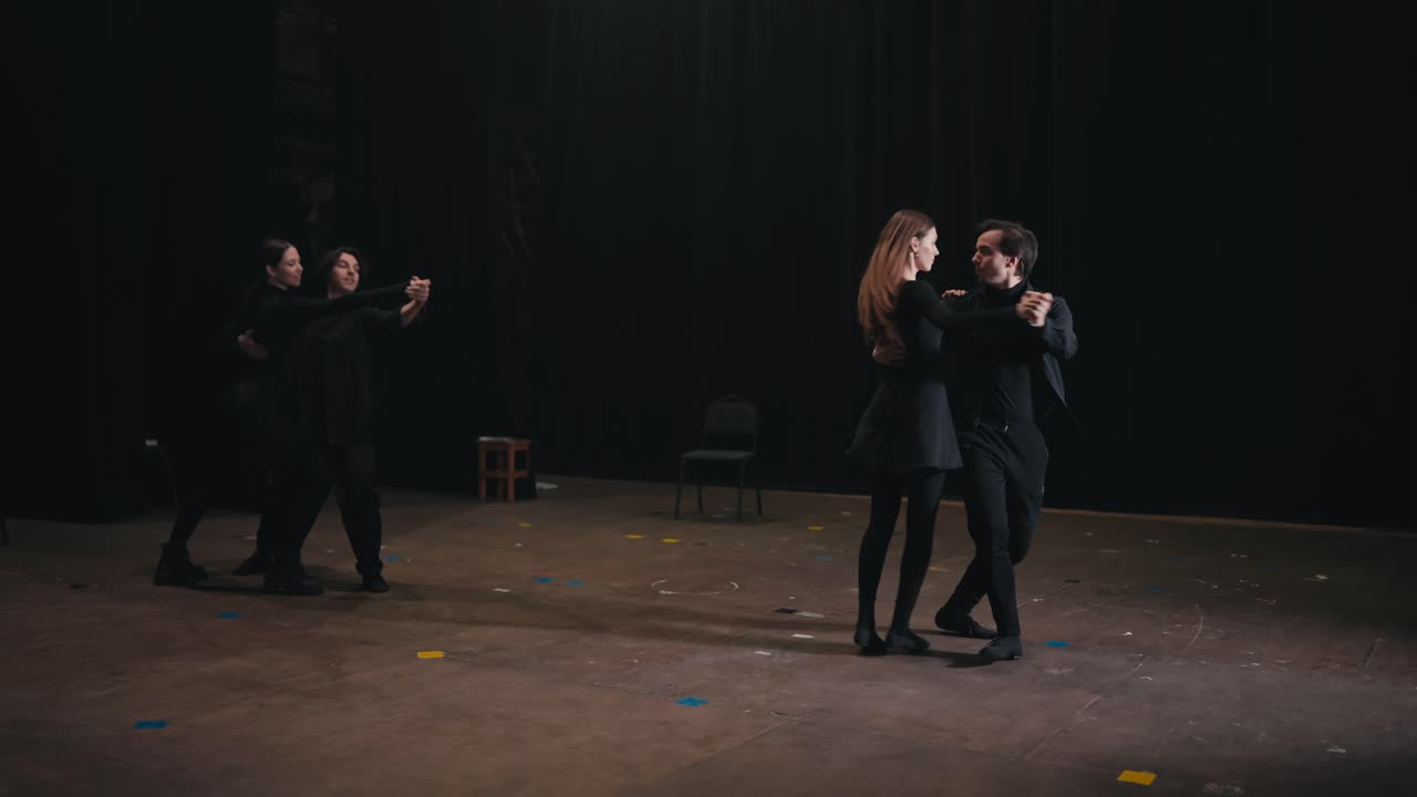 Two pairs of actors in black suits dance a slow dance and rehearse their act on stage before a performance in the theater. Beautiful slow dance as the finale of the actors performance on stage