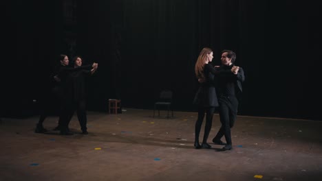 dos pares de actores en trajes negros bailan una danza lenta y ensayan su acto en el escenario antes de una actuación en el teatro. hermosa danza lenta como el final de la actuación de los actores en el escenario