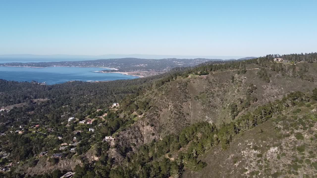수평선에 아름다운 푸른 만이 있는 임업 언덕에 있는 작은 마을, 높은 각도의 드론 전망