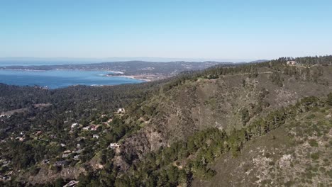 pequeña ciudad en la ladera forestal con una hermosa bahía azul en el horizonte, vista de drones de gran ángulo