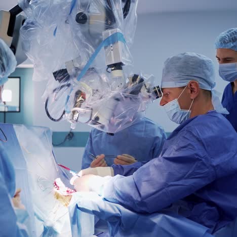 professional neurosurgeon looks through the microscope. medical equipment in surgery. group of doctors in medical uniform in the operating room.