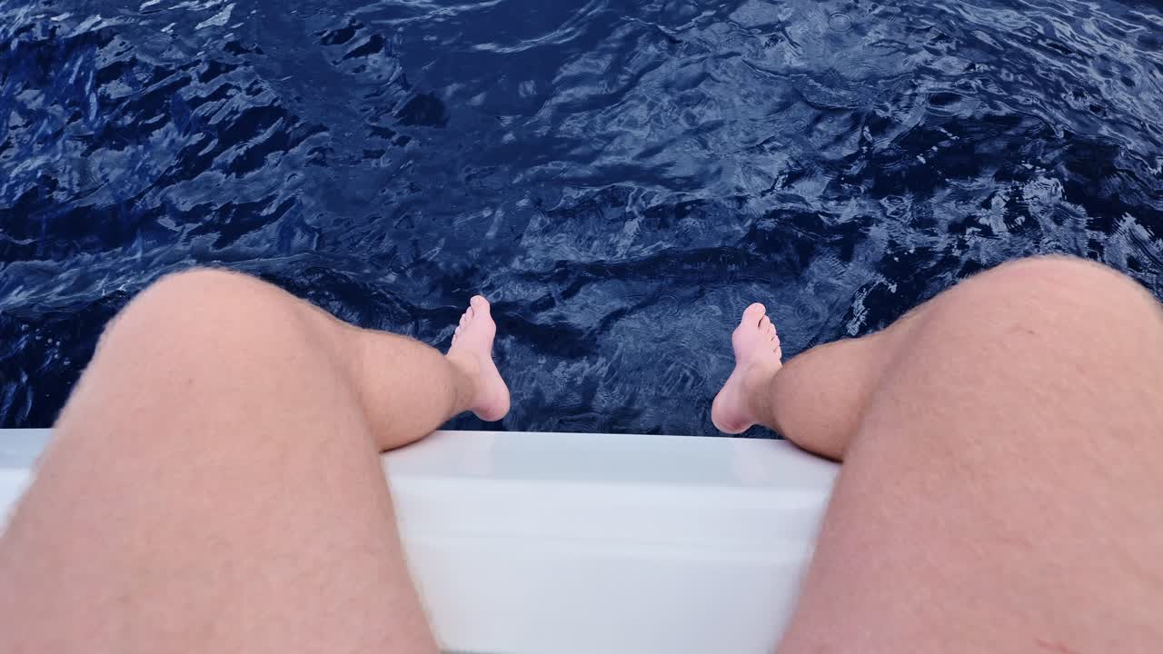 Close-up of man legs on boat, overlooking deep blue sea and foaming waves below