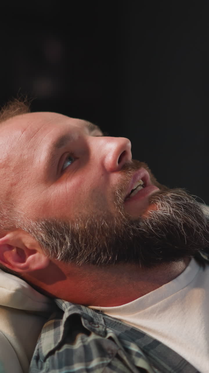 Bearded man takes comfortable pose on sofa to take rest and sleep. Male with bald patches having cardiac disease relaxes in living room at home close view