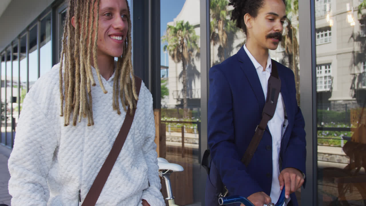 dos amigos varones diversos caminando juntos en bicicletas de ruedas en la calle