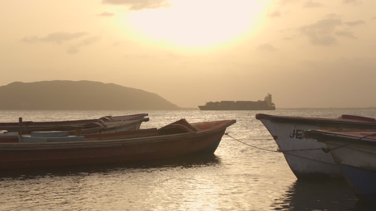 viejos barcos de pesca en port royal al atardecer con portacontenedores en segundo plano.
