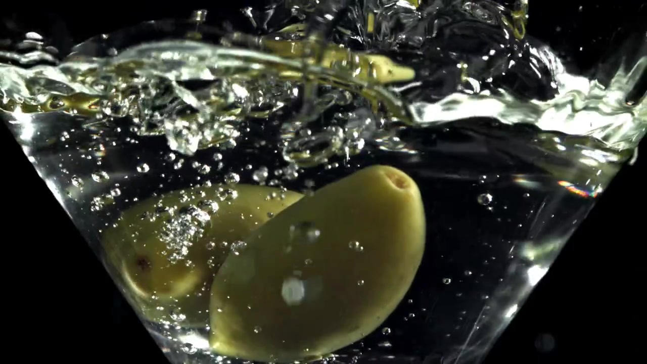 Olive verdi che cadono e schizzano in un bicchiere da Martini al rallentatore