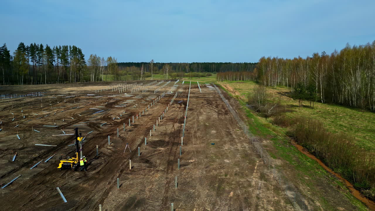 A field cleared and posts being installed to construct a solar panel grid - pullback aerial reveal