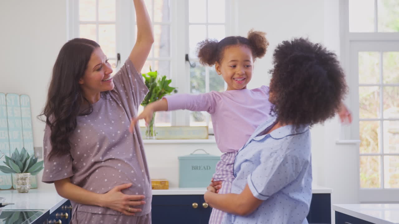 Família Grávida com Duas Mães Dançando e Fazendo Panquecas Matinais na Cozinha com a Filha