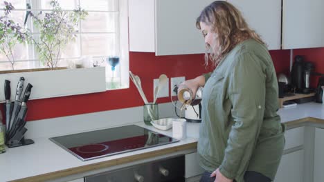 Caucasian-woman-wearing-green-shirt-and-preparing-coffee-in-kitchen