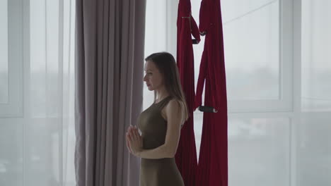 side view spiritual mentor practicing quietness in spa overlooking red silk hammocks wearing brown leggings focusing on mindfulness balance under soft ambient light reflecting inner calm presence
