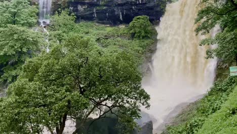 a stunning drone view of koltembha waterfall cascading down rocky cliffs, surrounded by lush green mountains and dense forests in bhandardara maharashtra india 4k