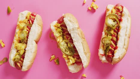 Video-of-hot-dogs-with-mustard,-ketchup-and-jalapeno-on-a-pink-surface