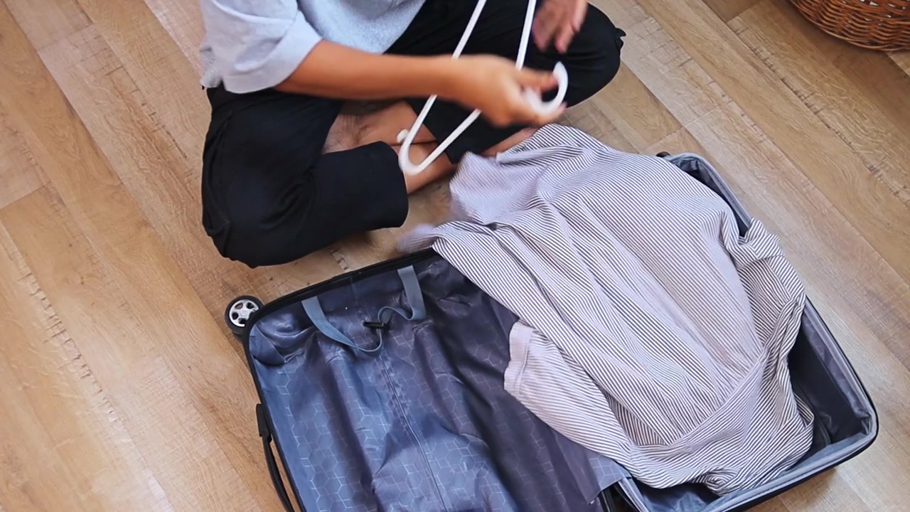 High-angle view of Person taking striped shirt off hanger and placing it inside case on floor