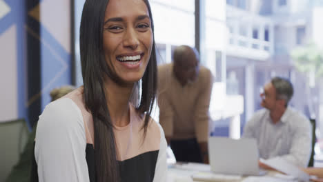 Portrait-of-happy-biracial-businesswoman-over-diverse-business-colleagues-discussing