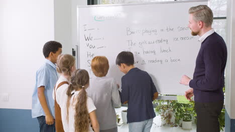 multiethnic students group and teacher standing in front of the blackboard while a student point out the verb to be