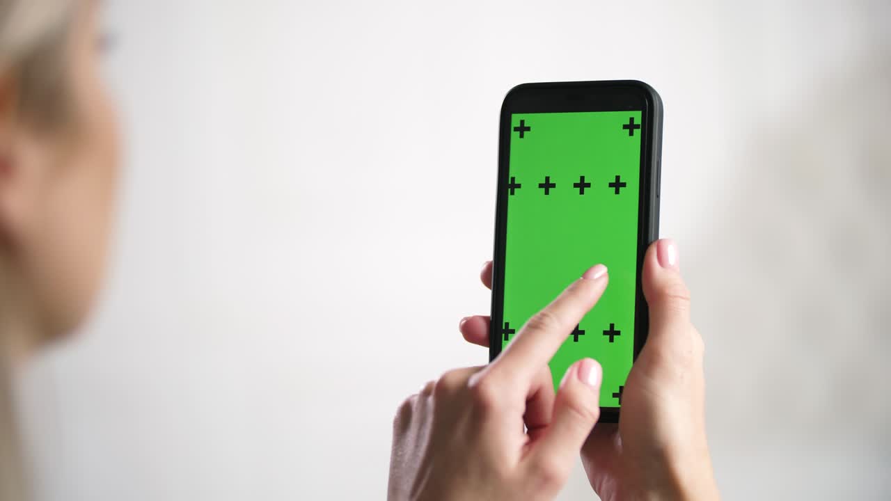 소녀는 손에 아이폰을 들고 스와이프를 하고, 녹색 모형 크로마키 광고 화면을 슬라이드합니다.