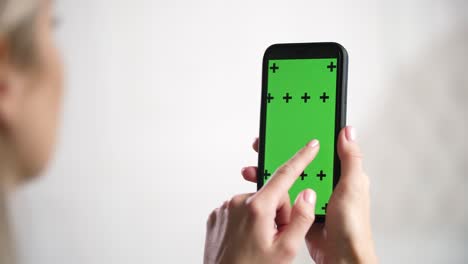 la chica tiene en las manos el iphone y desliza, desliza la pantalla de anuncios de chromakey de maqueta verde.