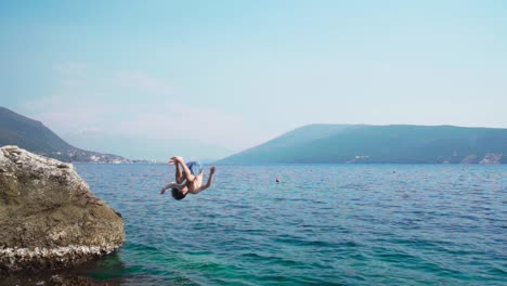 Caucasian-young-boy-jumping-into-sea-from-a-rock-in-slow-motion-doing-somersault