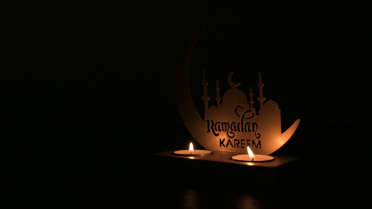 Mani che accendono candele su decorazioni del Ramadan con silhouette di moschea in ambiente buio