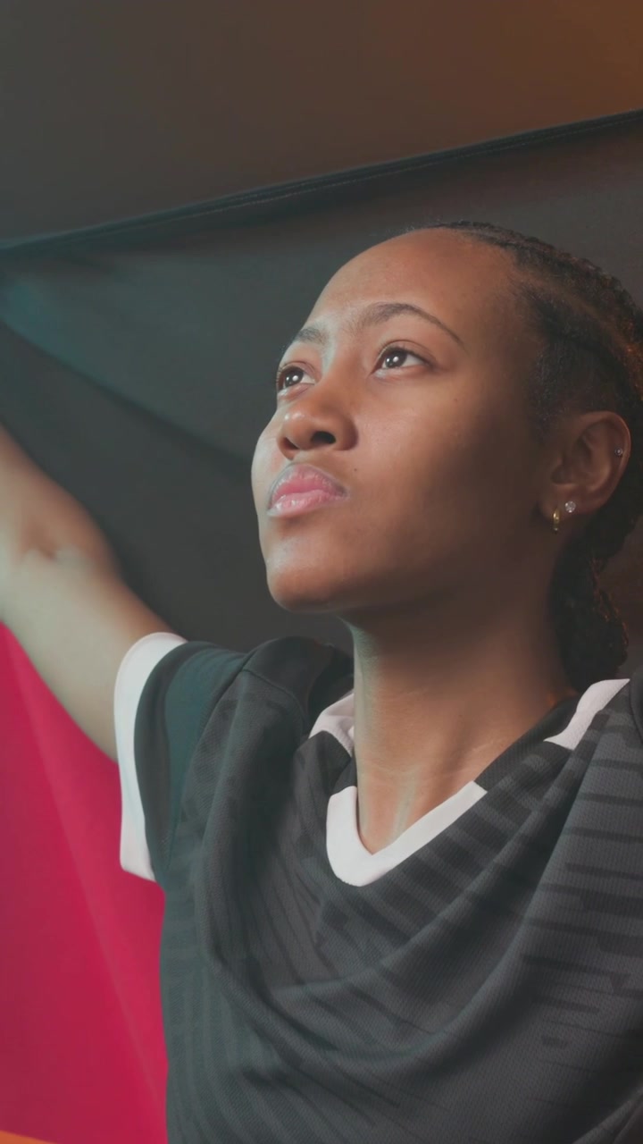 Vertical video: Lifting flag from below, woman in black shirt raising it posing in studio with clip