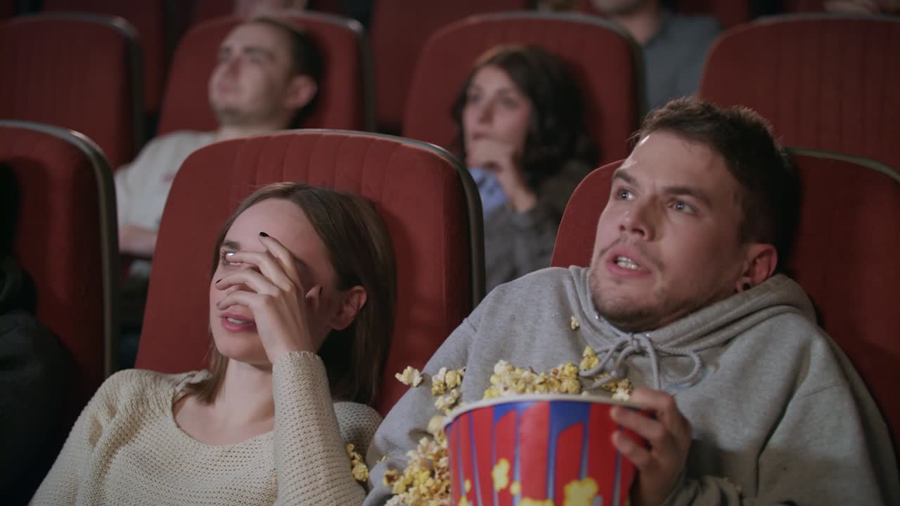 una joven pareja viendo una película de terror en el cine. un tipo rociando palomitas de maíz