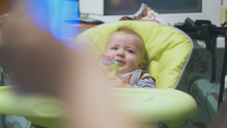 person shows shining toy to funny baby resting in highchair