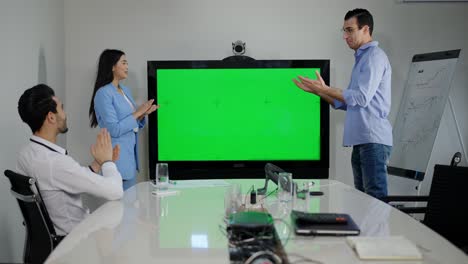 tomada amplia de la oficina con el monitor chromakey y un grupo de alegres colegas multirraciales haciendo gestos de victoria y aplaudiendo. millennials positivos y alegres regocijándose del éxito de la startup.
